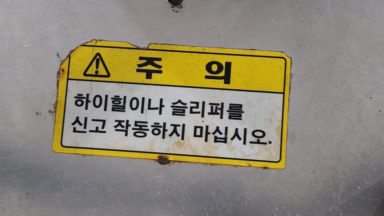 Sticker with a warning in Korean: "Caution, do not operate while wearing high heels or slippers."