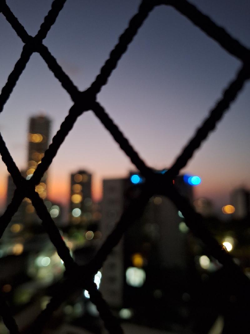 Fotografia desfocada de uma cidade vista por uma tela em uma janela, destacando a paisagem urbana ao redor.